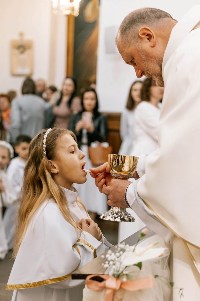 Retrato de una niña recibiendo la comunión de manos del cura en una iglesia, fotografía de Daniel Hubscher